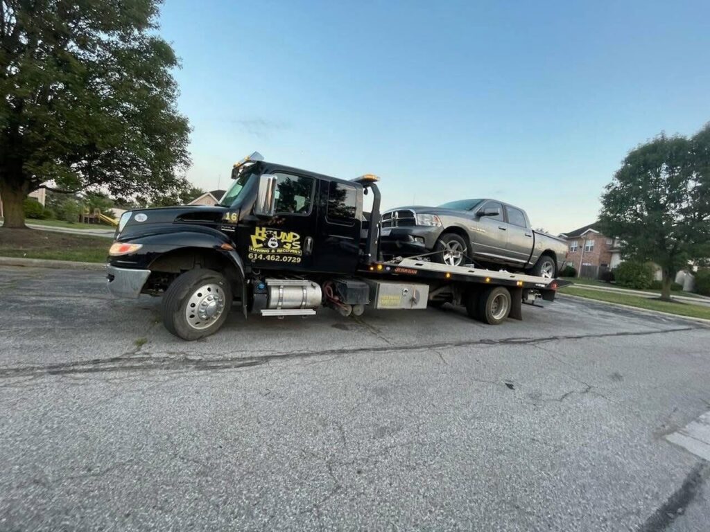 A Hound Dog's Towing & Recovery flatbed tow truck towing a grey pickup truck in Columbus, OH.
