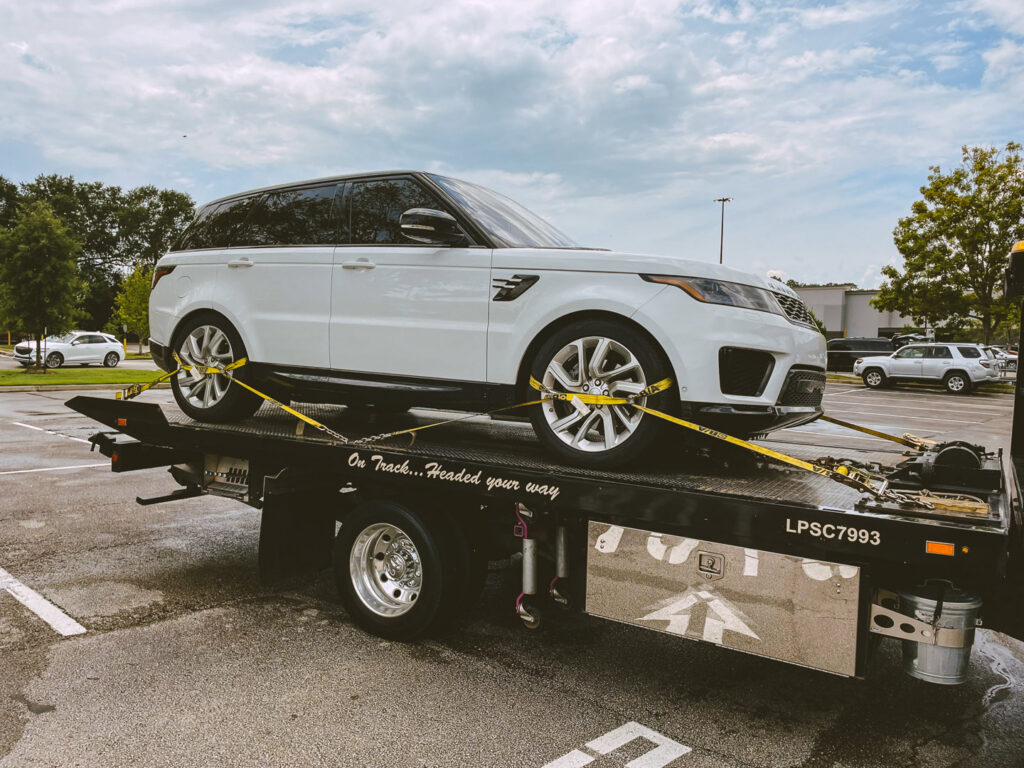 A flatbed tow truck from Rosco's Towing Services LLC towing a white Range Rover SUV in Carencro, LA.