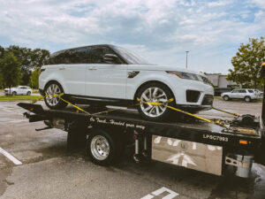 A flatbed tow truck from Rosco's Towing Services LLC towing a white Range Rover SUV in Carencro, LA.