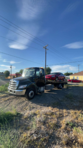 A black flatbed tow truck from A&R towing LLC transporting a red sedan in Nampa, ID.