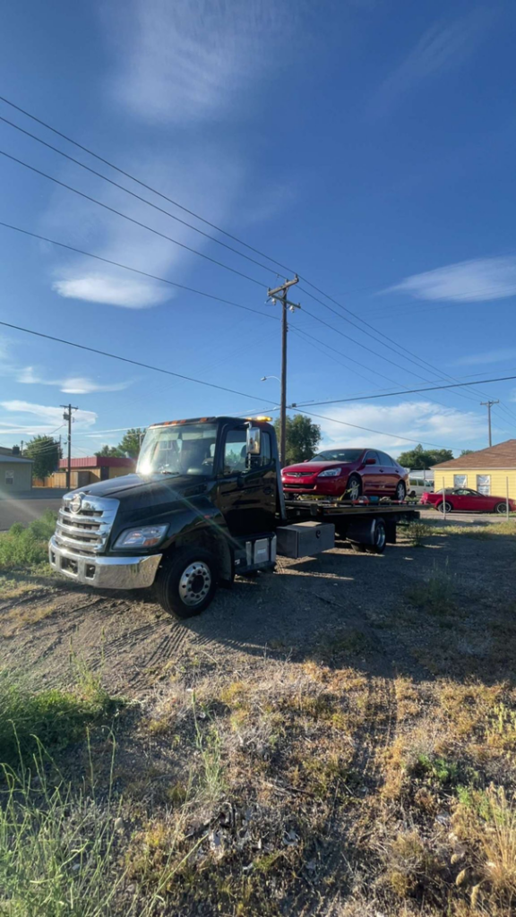 A black flatbed tow truck from A&R towing LLC transporting a red sedan in Nampa, ID.