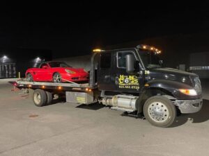 A Hound Dog's Towing & Recovery flatbed tow truck towing a red sports car at night in Columbus, OH.
