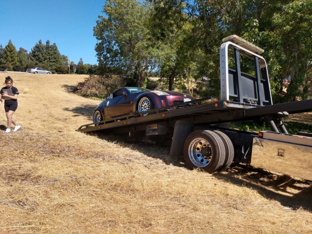 Aguilar Towing's flatbed tow truck transporting a purple sports car from a grassy slope in San Jose, CA