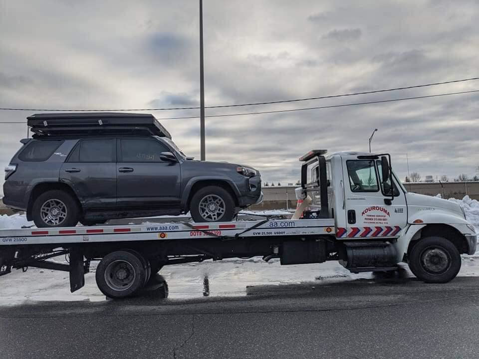 A Kourouma Towing Services flatbed tow truck transporting a dark grey SUV in Philadelphia, PA.