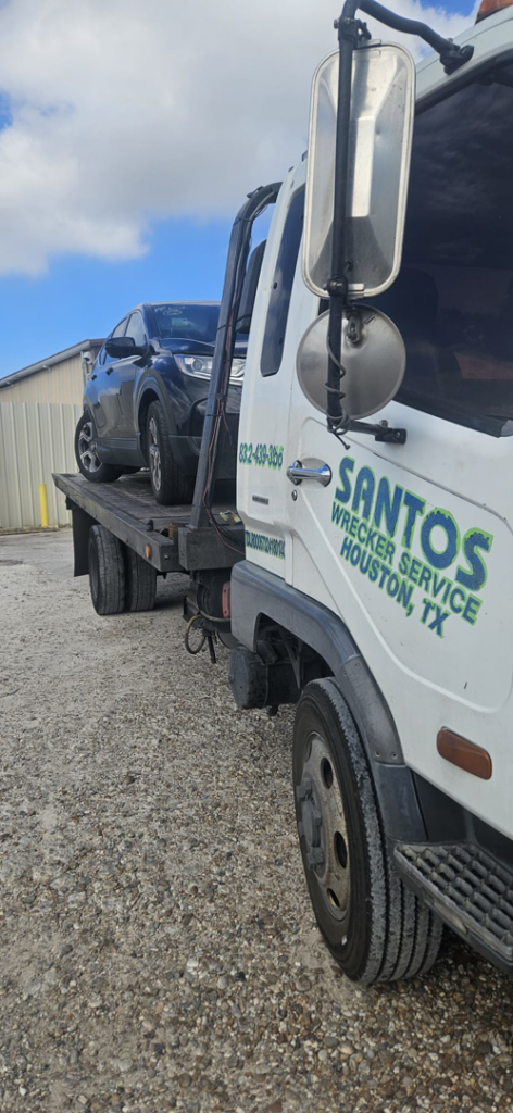A flatbed tow truck from Santos Wrecker Services in Houston, TX, transporting a dark SUV.