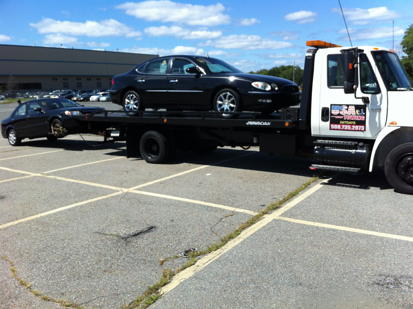 A flatbed tow truck is transporting two cars for USA Towing, Recovery and Storage in Worcester, MA