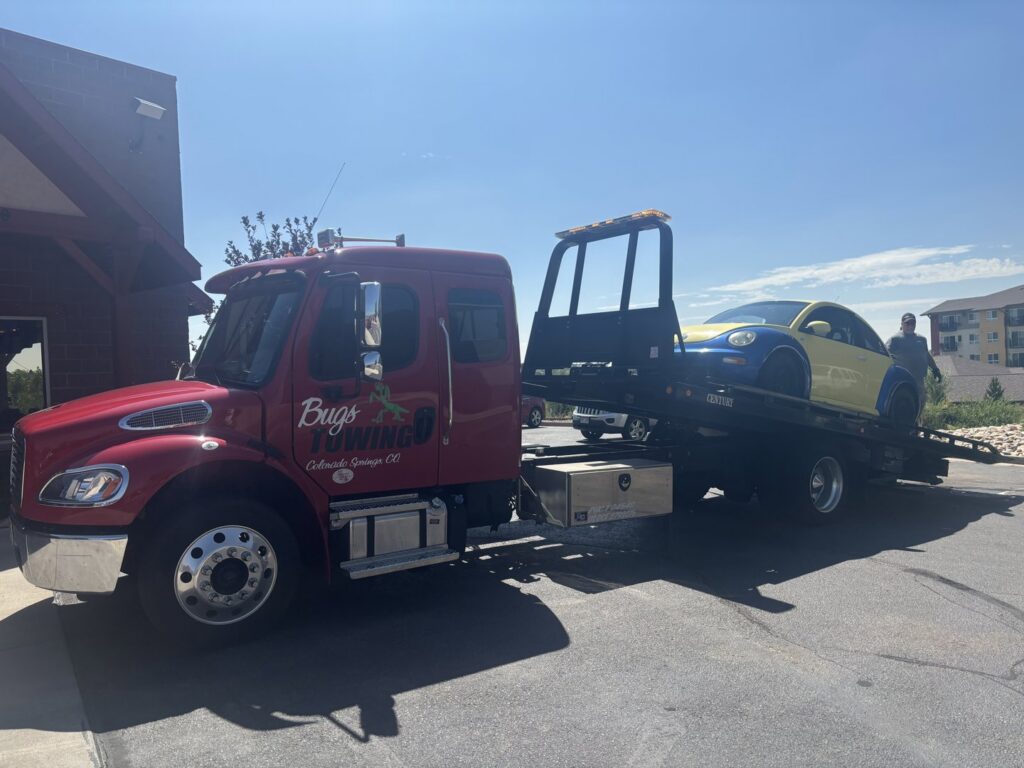 A flatbed tow truck from Towing Colorado transporting a yellow and blue Volkswagen Beetle in Colorado Springs, CO.