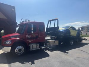 A flatbed tow truck from Towing Colorado transporting a yellow and blue Volkswagen Beetle in Colorado Springs, CO.