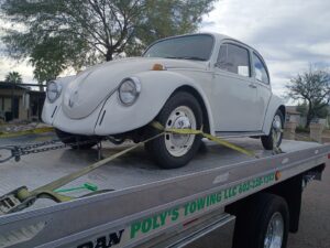 A white classic Volkswagen Beetle loaded on a flatbed tow truck from Poly's Towing Glendale, AZ.