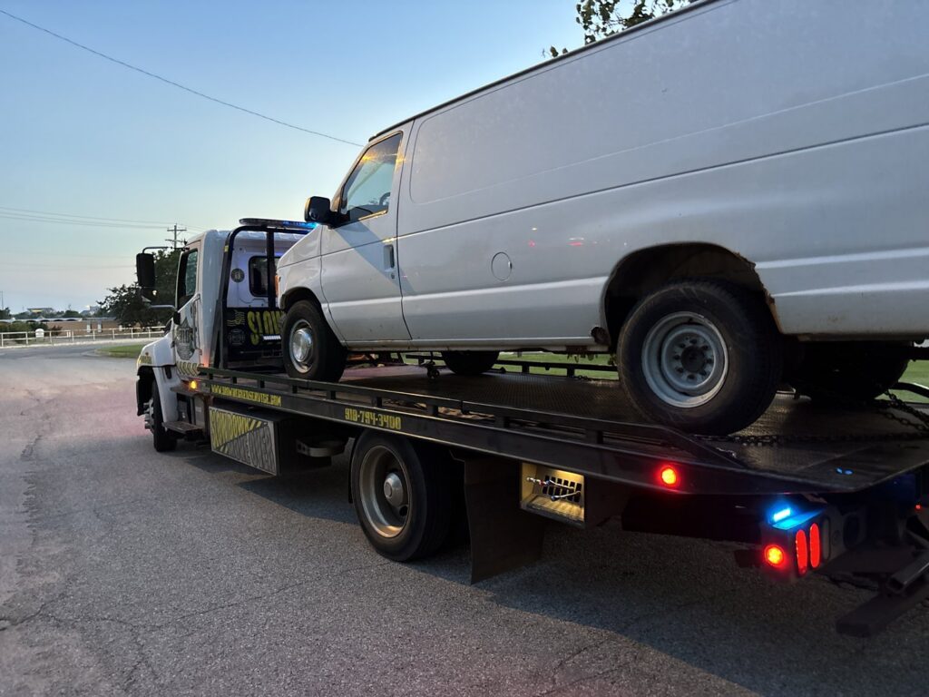 A flatbed tow truck from 918 Wrecker Service transporting a white van in Tulsa, OK.