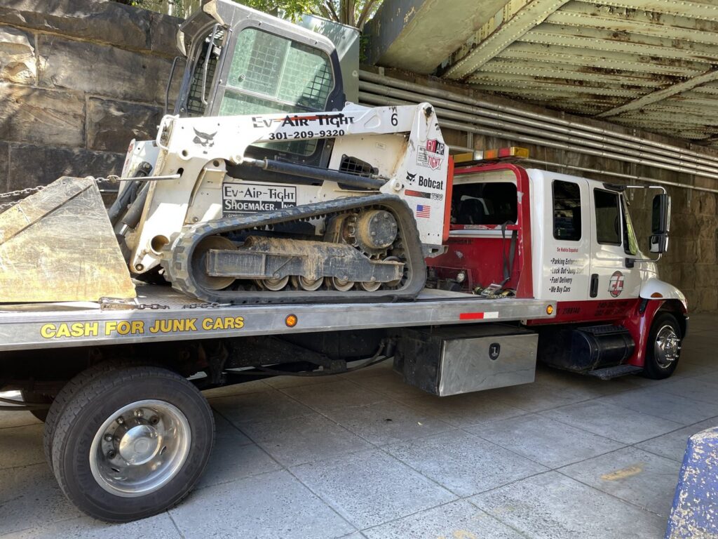 An E.C. Towing, Inc. flatbed tow truck transporting a Bobcat skid-steer loader in Gaithersburg, MD.