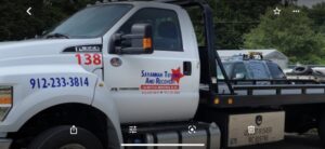 A white flatbed tow truck from Savannah Towing And Recovery transporting a car on its bed in Savannah, GA.