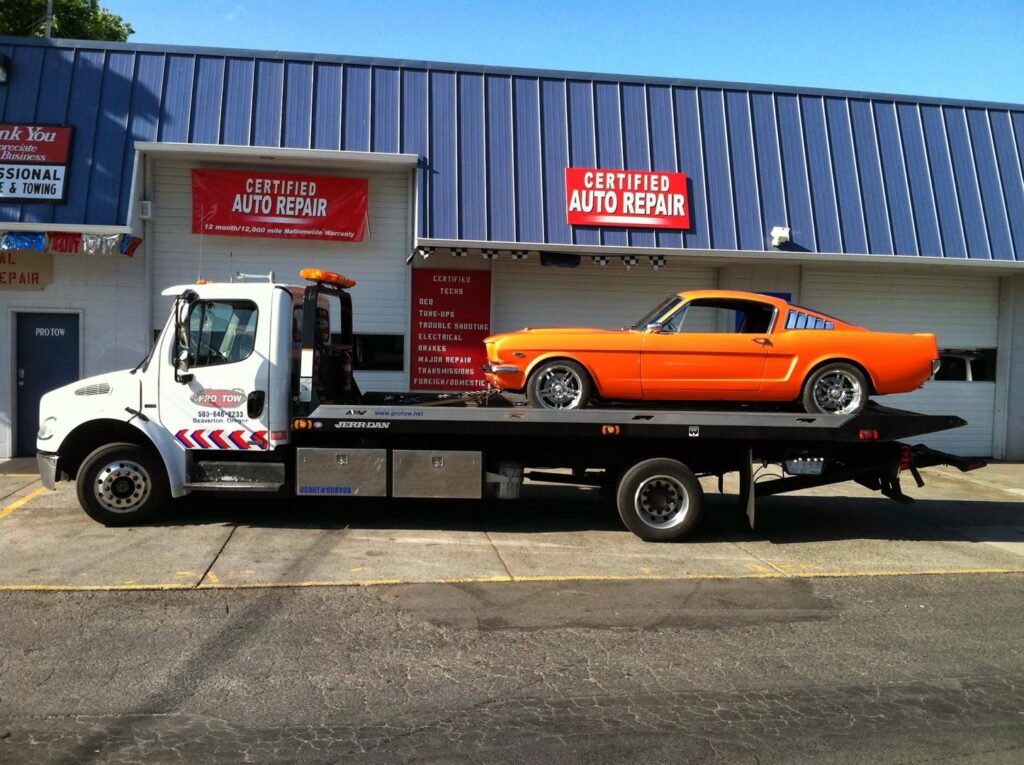 A PRO TOW flatbed tow truck transporting a classic orange car in Beaverton, OR.