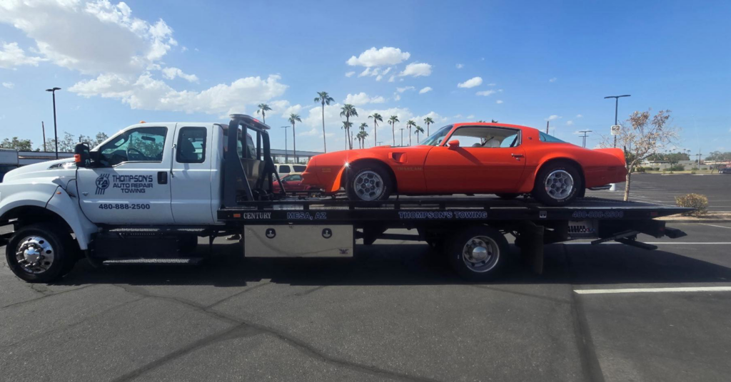 A Thompson's Auto Repair & Towing flatbed tow truck transporting an orange classic car in Mesa, AZ.