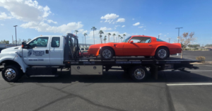 A Thompson's Auto Repair & Towing flatbed tow truck transporting an orange classic car in Mesa, AZ.