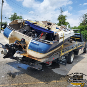 A flatbed tow truck from Sunny Acres Towing transporting a damaged boat in Greenville, IN.