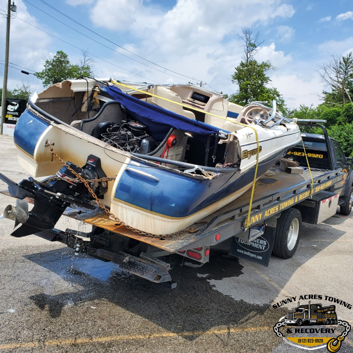 A flatbed tow truck from Sunny Acres Towing transporting a damaged boat in Greenville, IN.