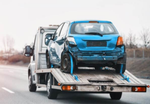 A flatbed tow truck transporting a severely damaged blue car for Rapt Roadside & Towing Services in Jacksonville, FL.