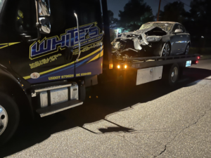 A White's Wrecker Service flatbed tow truck transporting a severely damaged car at night in Memphis, TN.
