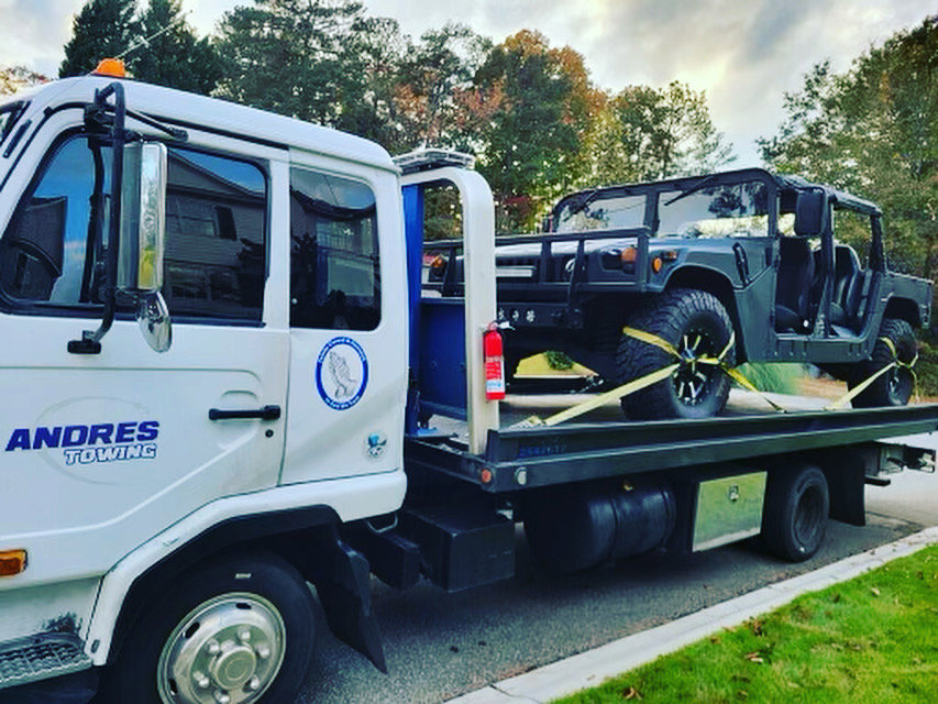 A white flatbed tow truck from Andre's Towing Services, LLC transporting a dark green Hummer in Marietta, GA.