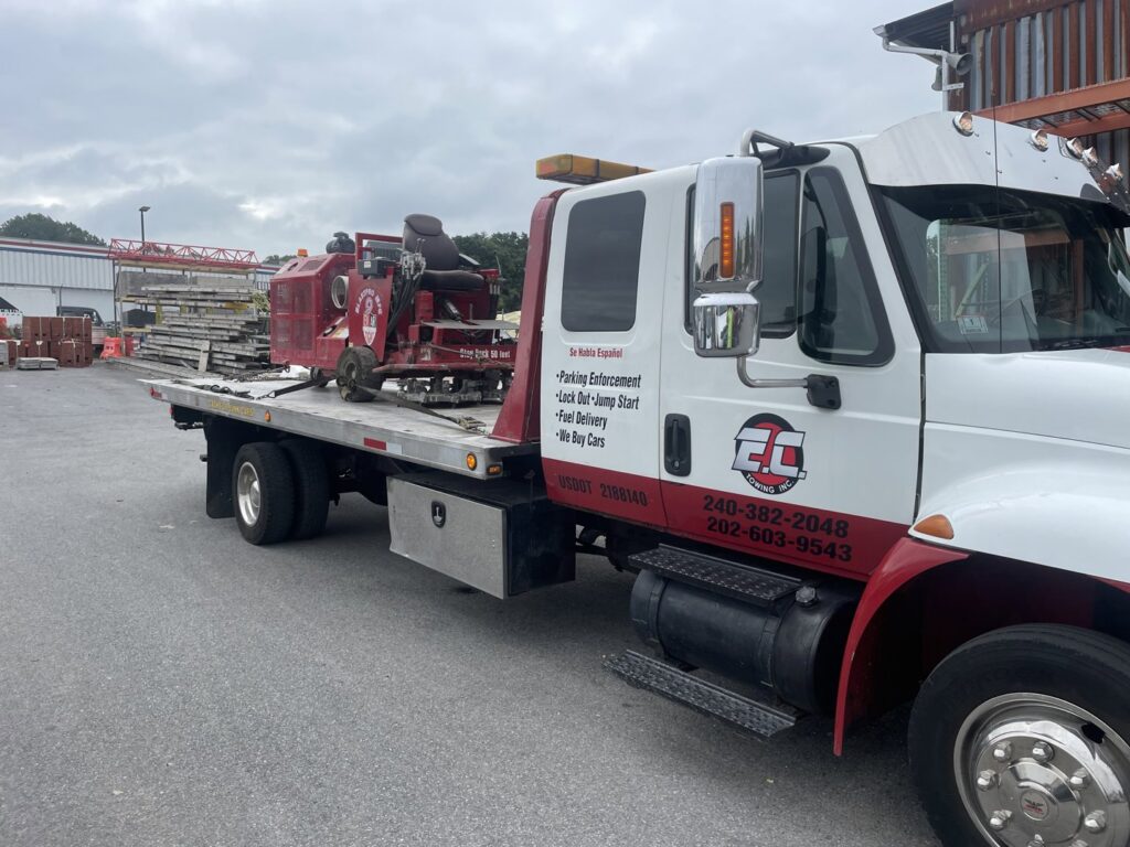 An E.C. Towing, Inc. flatbed tow truck transporting heavy equipment in Gaithersburg, MD.