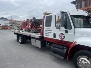 An E.C. Towing, Inc. flatbed tow truck transporting heavy equipment in Gaithersburg, MD.