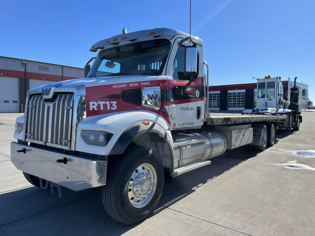 A flatbed tow truck from MAD J Repair & Towing transporting a piece of equipment in Des Moines, IA.