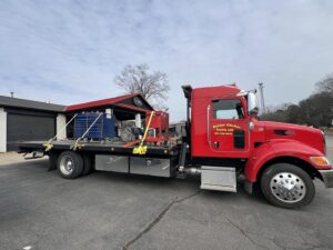 A red flatbed tow truck from Rubber Chicken Towing LLC transporting equipment, including toolboxes, in Charlotte, NC.