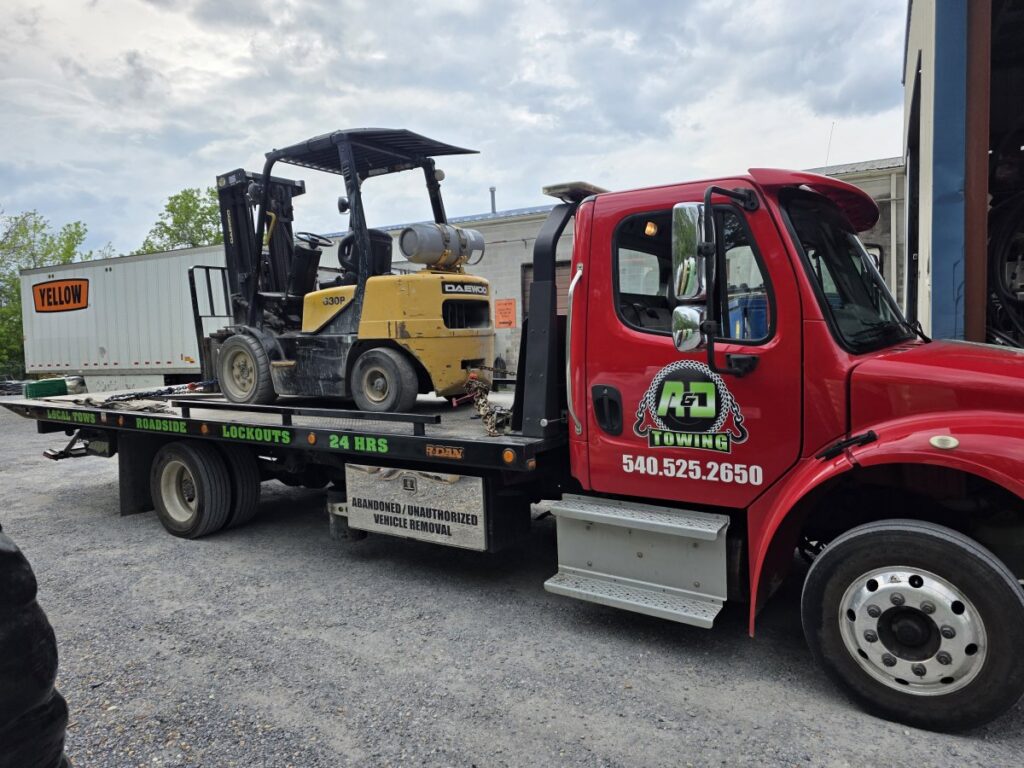 A red flatbed tow truck from A and D Towing is transporting a yellow forklift in Little Ferry, NJ.