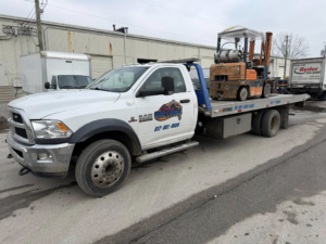 A white flatbed tow truck from Danny's Towing Edgar transporting a forklift in Indianapolis, IN.