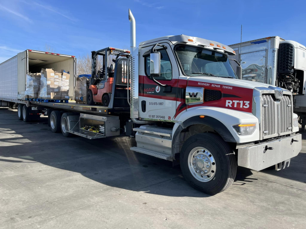 A flatbed tow truck from MAD J Repair & Towing transporting a forklift in Des Moines, IA.