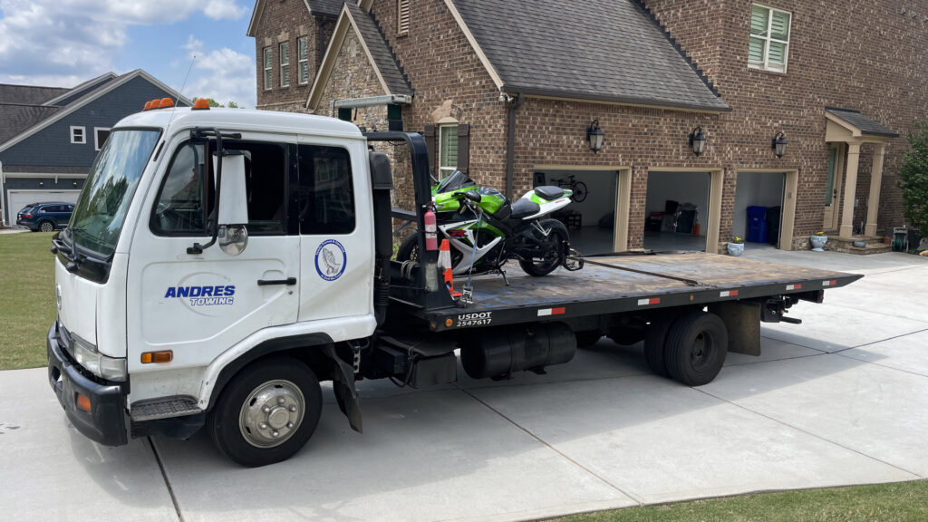 A white flatbed tow truck from Andre's Towing Services, LLC transporting a green motorcycle in Marietta, GA.