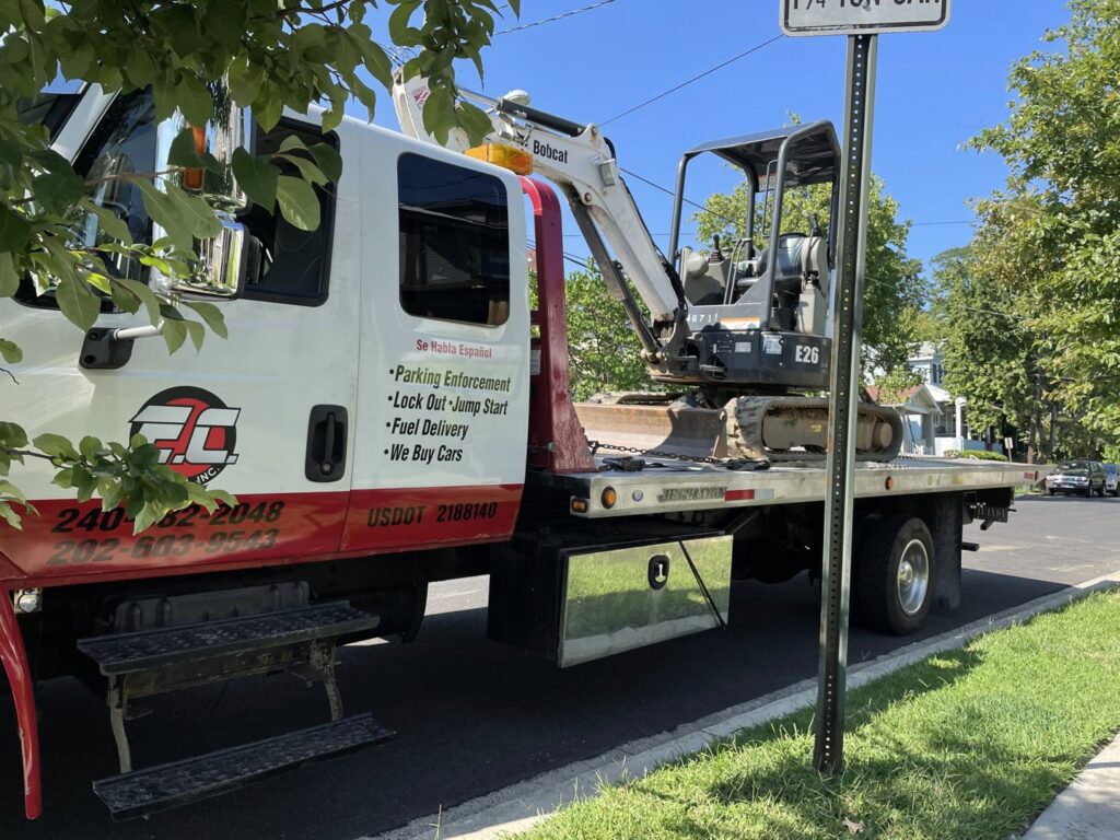 An E.C. Towing, Inc. flatbed tow truck transporting a mini excavator in Gaithersburg, MD.