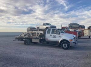 A ROMU Towing flatbed truck transporting multiple cars, parked in a lot in El Paso, TX.