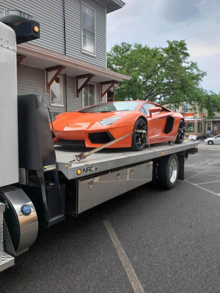 A flatbed tow truck from Bailey's Towing and Auto Body, LLC transporting an orange Lamborghini in Merrimack, NH.