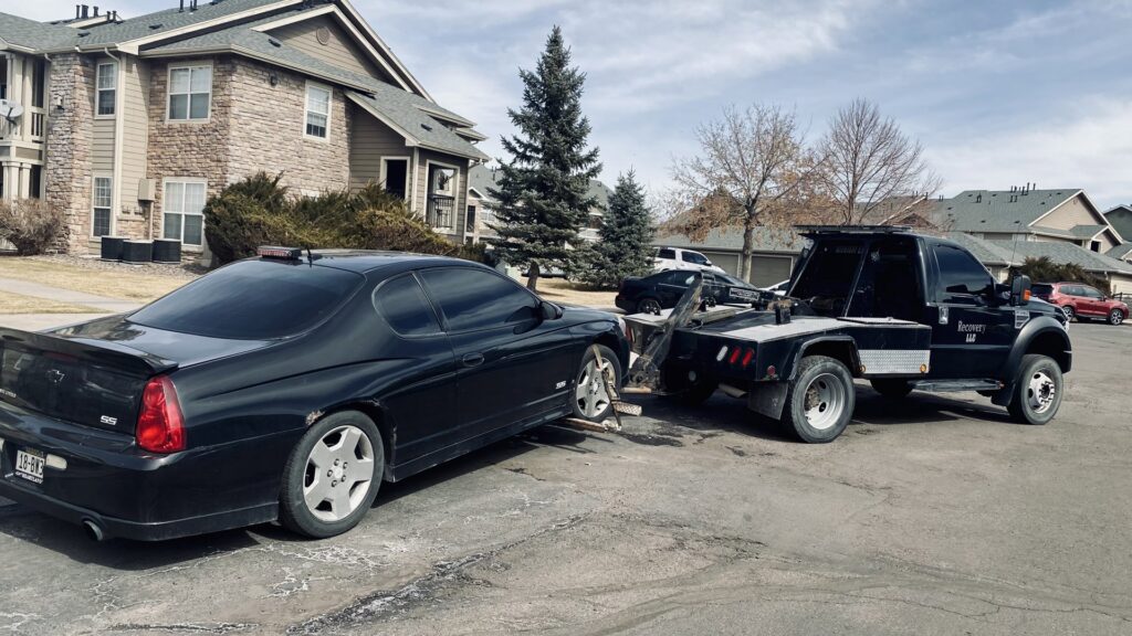 A flatbed tow truck from Henderson Towing & Recovery LLC transporting a red convertible car in Denver, CO.