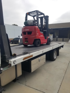 A flatbed tow truck from Leos Towing Service transporting a red forklift in Anaheim, CA.