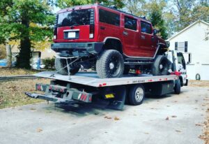 A white flatbed tow truck from Andre's Towing Services, LLC transporting a red Hummer H2 in Marietta, GA.