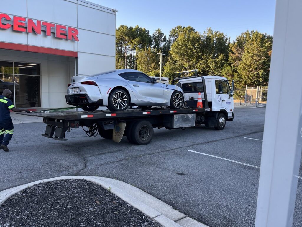 A white flatbed tow truck from Andre's Towing Services, LLC transporting a silver sports car in Marietta, GA.