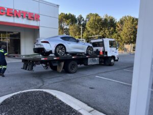 A white flatbed tow truck from Andre's Towing Services, LLC transporting a silver sports car in Marietta, GA.
