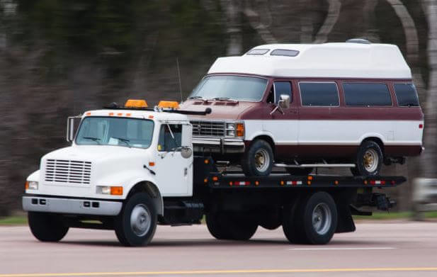 A flatbed tow truck transporting a classic van for Rapt Roadside & Towing Services in Jacksonville, FL.