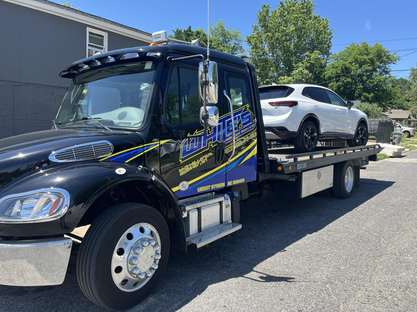 A White's Wrecker Service flatbed tow truck transporting a white SUV in Memphis, TN.