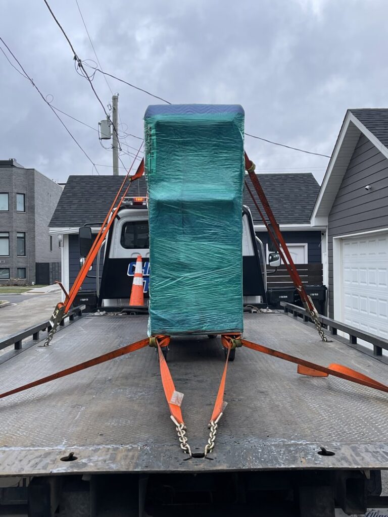 A flatbed tow truck from Chicago Towing transporting a large, wrapped piece of equipment in Chicago, IL.