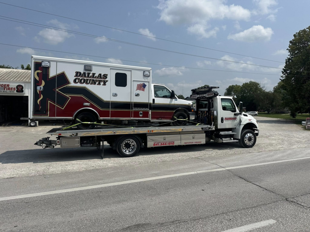 A flatbed tow truck towing an ambulance for Diversified Towing and Recovery, LLC in Creston, IA.