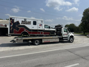 A flatbed tow truck towing an ambulance for Diversified Towing and Recovery, LLC in Creston, IA.