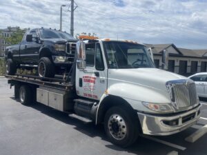 A white flatbed tow truck from Always Ready Towing transporting a black pickup truck in North Fort Myers, FL.