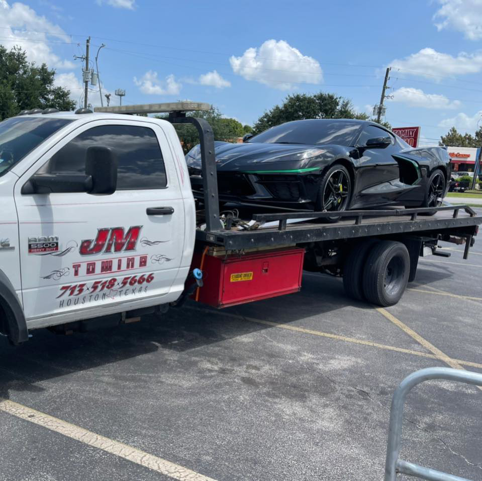 JM Towing & Transport LLC flatbed truck towing a black sports car in Houston, TX.