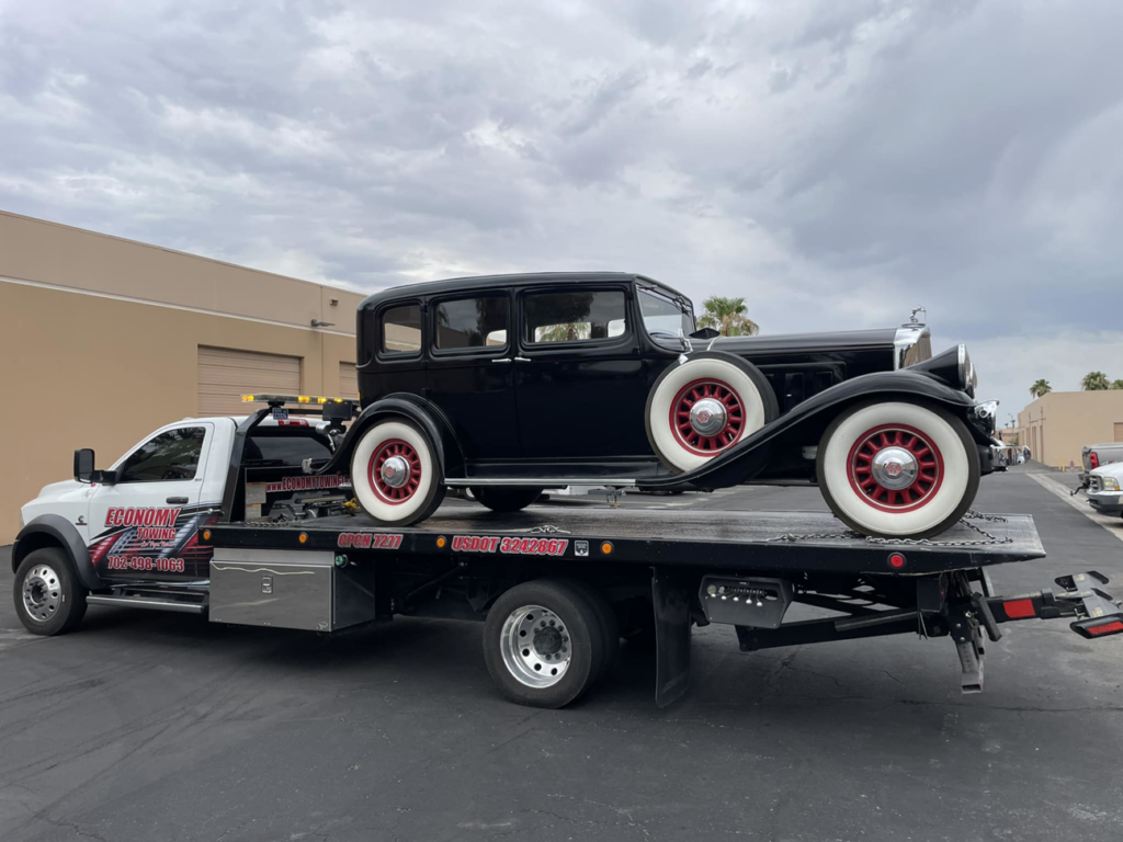 Economy Towing's flatbed truck transporting a classic black vintage car in Las Vegas, NV.