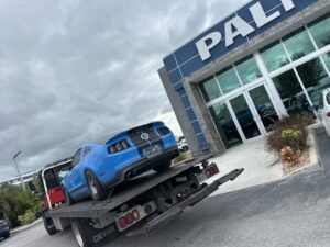 A flatbed tow truck from Rodicio Towing Services transporting a blue Ford Mustang in Hialeah, FL.