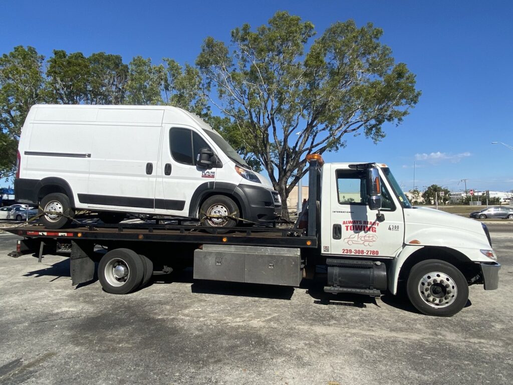 A white flatbed tow truck from Always Ready Towing transporting a white cargo van in North Fort Myers, FL.